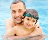 Smiling father and son leaning in the water pool